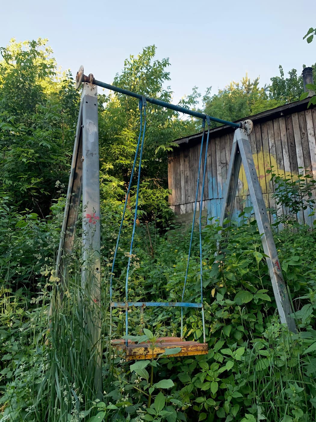 Le même terrain avant le chantier : un portique rouillé au milieu des ronces, un abri en bois au fond