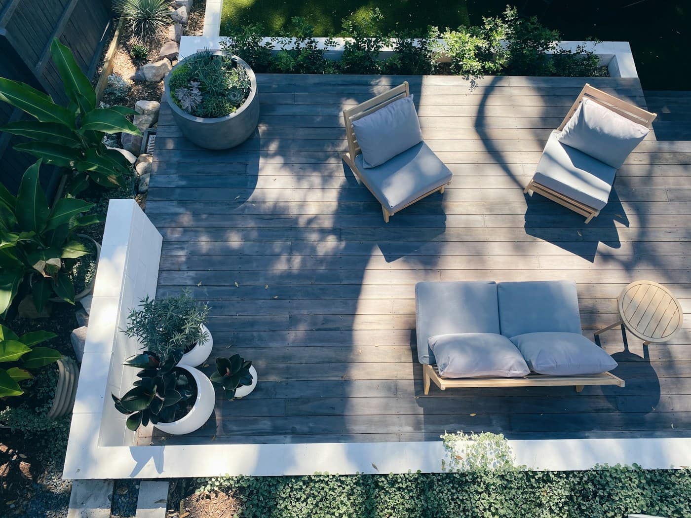 Terrasse en bois vue d'en haut, avec banquette, fauteuils et grands pots plantés